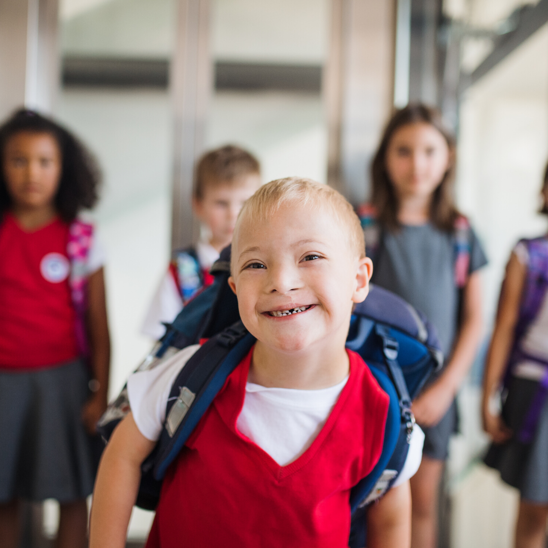 Young boy with school bag in school hallway with friends