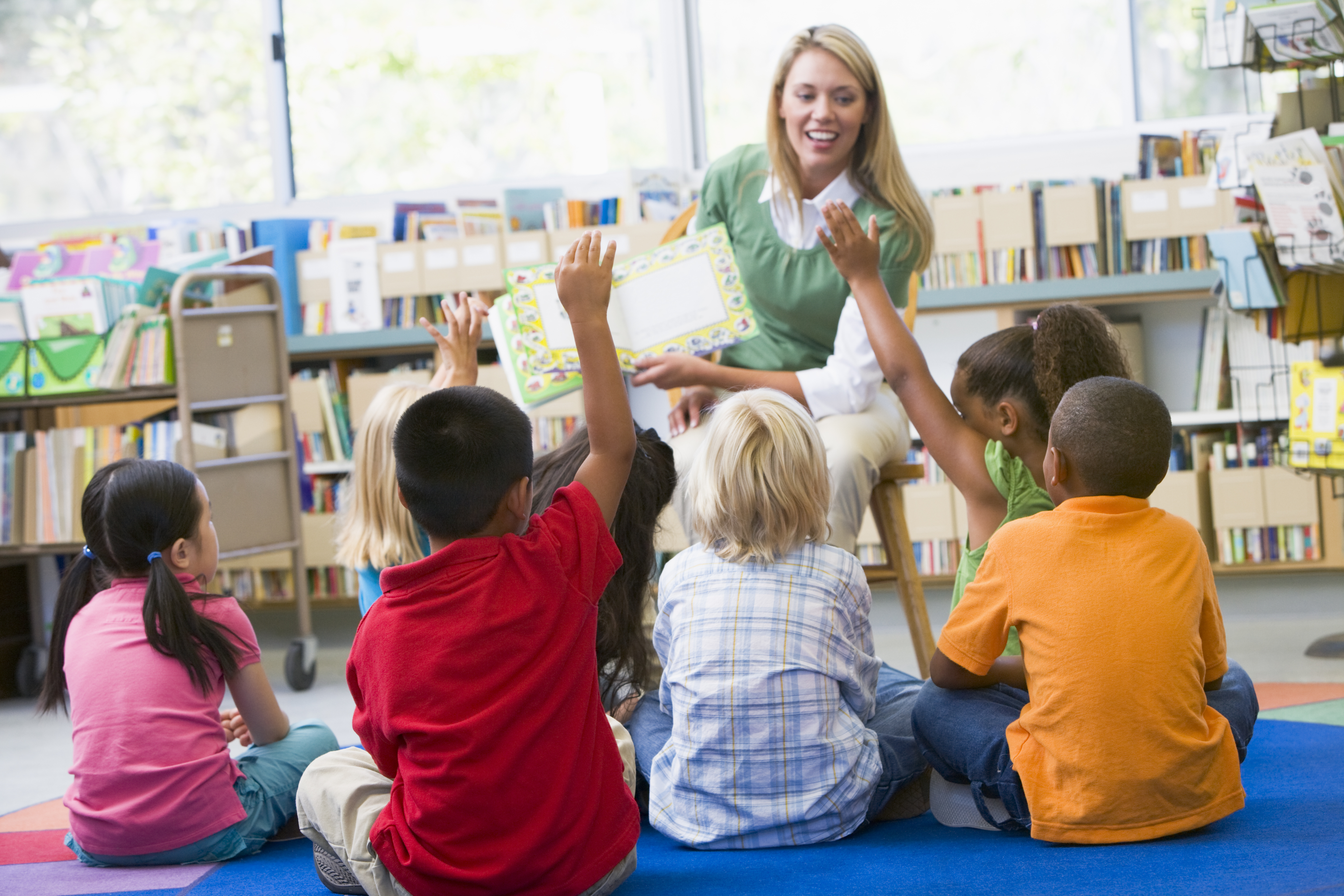 library stock image 3 Young children seated on floor at a public library with librarian reading a story