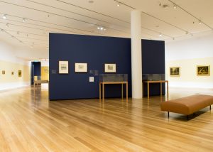 Image shows interior of art gallery with paintings on display