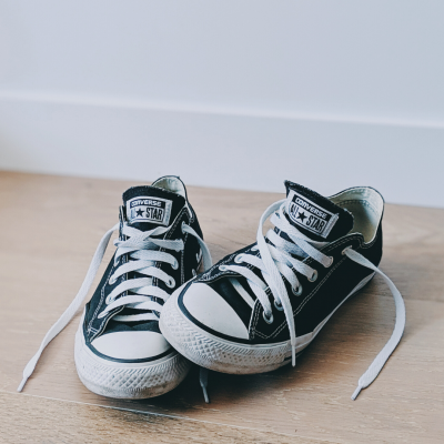 Pair of black converse shoes sitting on wooden floor with laces untied