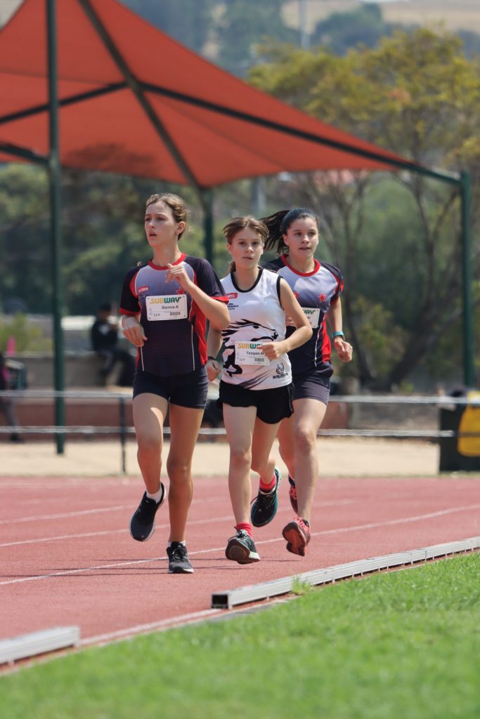 Three young girls dressed in athletic gear running on an athletics track