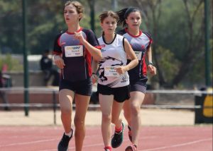 Three young girls dressed in athletic gear running on an athletics track
