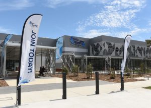 Exterior front entrance to Gurri Wanyarra Wellbeing Centre with branded flags and a blue sky