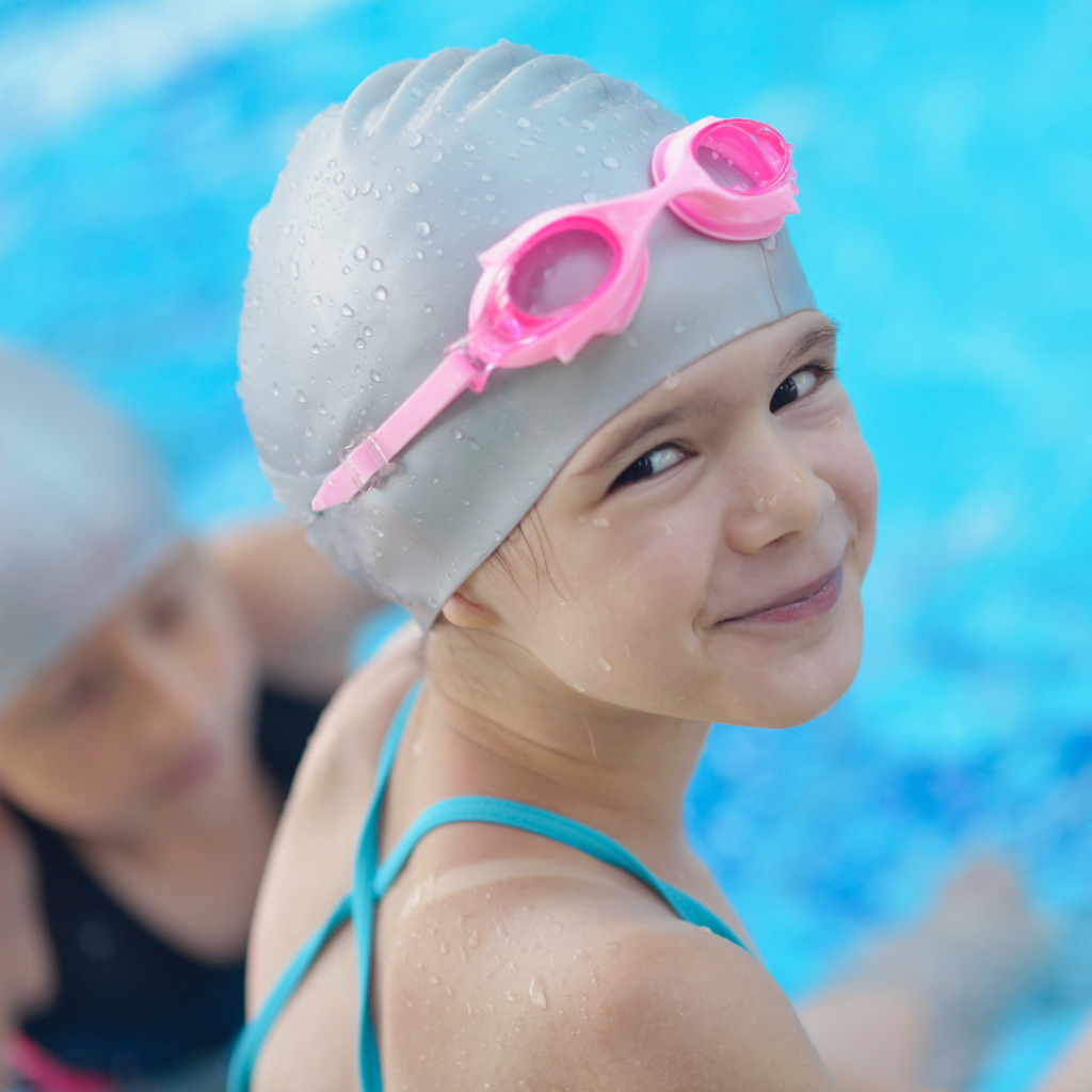 swim Young girl wearing bathers, swimming cap and goggles sitting on edge of pool