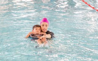 Swimming instructor in the water teaching child to swim on back.