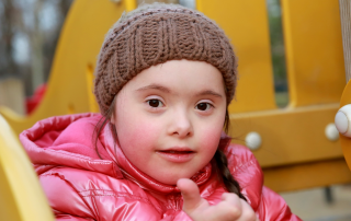 Young girl with down syndrome giving thumbs up and playing at outdoor playgound