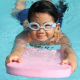 Young girl swimming in the water wearing swimwear and goggles and holding a kickboard