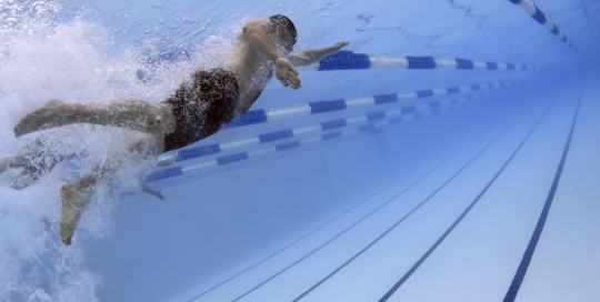 Swimming pool underwater photo looking toward the surface with a swimmer and lane ropes