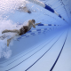 Swimming pool underwater photo looking toward the surface with a swimmer and lane ropes