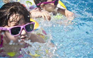 Two young children in swimwear and goggles playing in an outdoor pool