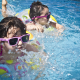 Two young children in swimwear and goggles playing in an outdoor pool