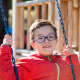 Young boy wearing red jacket and glasses playing on a swing in an outdoor playground