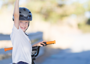 Young child stationary on bike facing the camera with arm in air