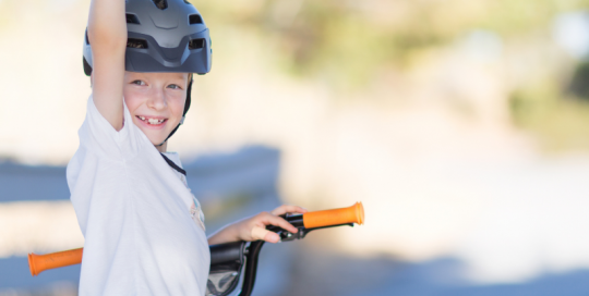 Young child stationary on bike facing the camera with arm in air