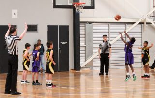 Team of young children in sports uniform playing a game of basketball on an indoor stadium with two referees looking on
