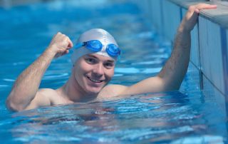 Male swimmer in water wearing swimwear in swimming pool at edge of pool