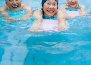 Three older people in a swimming pool wearing swimwear and holding kickboards