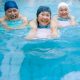 Three older people in a swimming pool wearing swimwear and holding kickboards