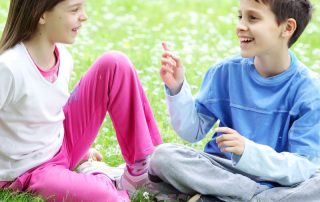 Two children, a girl and a boy, sitting on grass engaging in coversation and both smiling