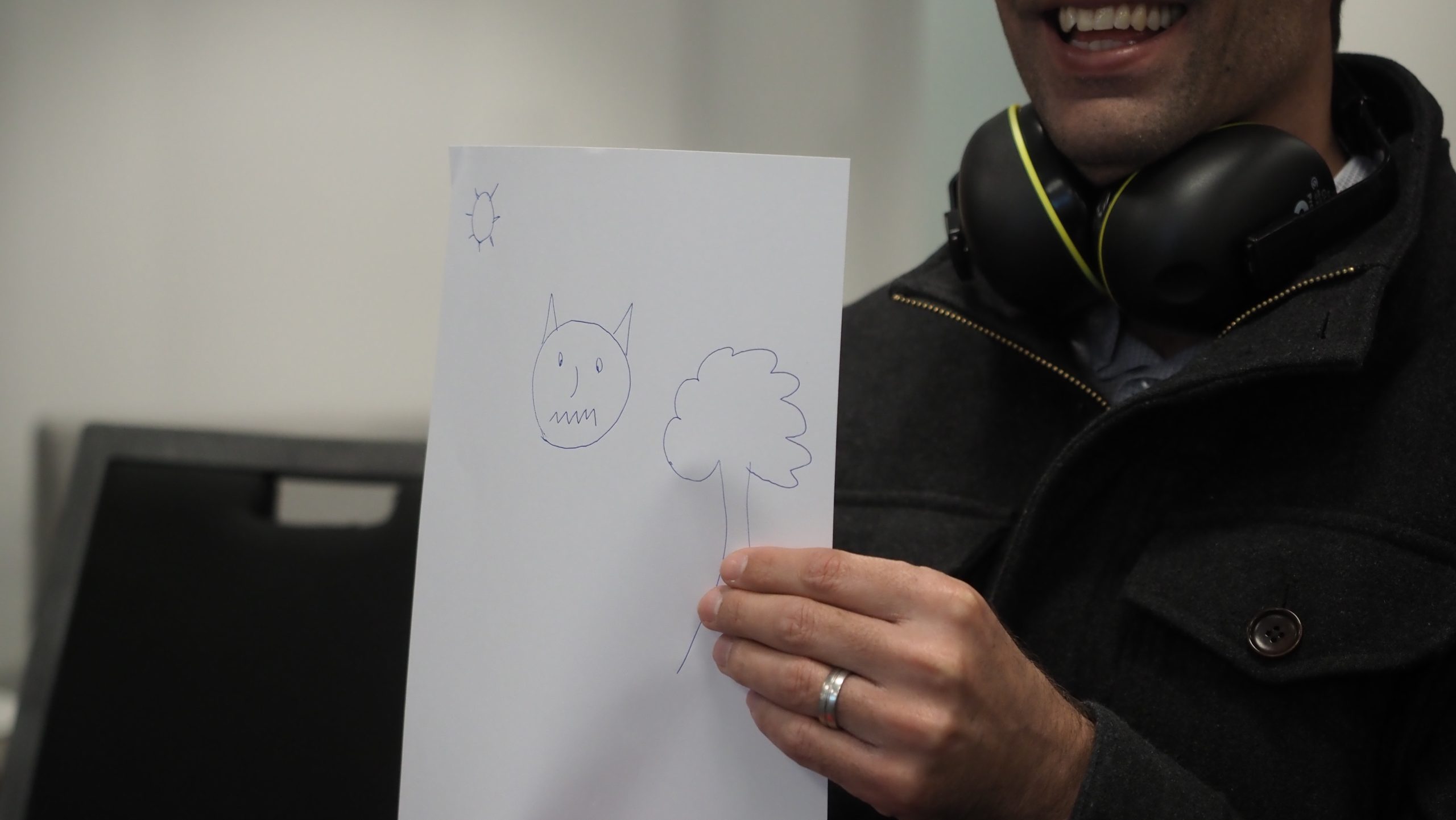 Smiling face of man holding up white piece of paper with drawing on it