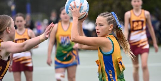 Two girls netball teams playing a game on a court