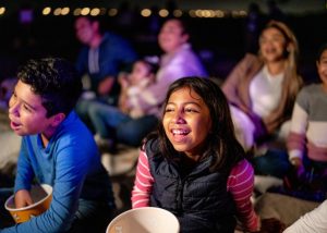 Children seated outdoors with popcorn watching a movie