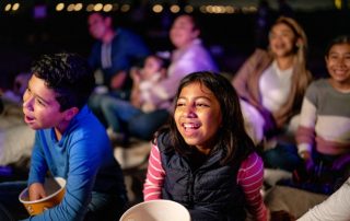 Children seated outdoors with popcorn watching a movie